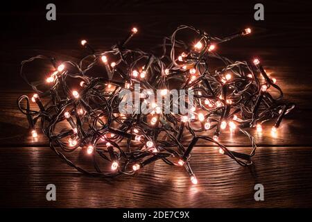 Scintillanti luci natalizie su un tavolo di legno scuro. Decorazioni illuminanti con lampi a LED in un'oscurità. Vacanze invernali Natale e Capodanno. Foto Stock