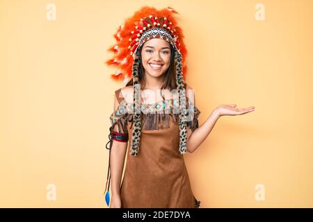 Giovane bella ragazza latina che indossa costume indiano sorridente allegro presentazione e puntando con palmo di mano guardando la fotocamera. Foto Stock