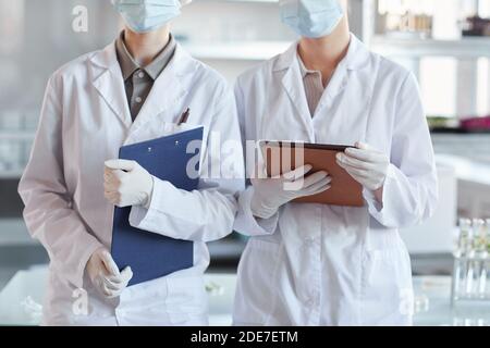 Ritratto troncato di due scienziati donne che indossano la maschera facciale e. tenere le lavagne mentre si è in piedi in laboratorio medico Foto Stock