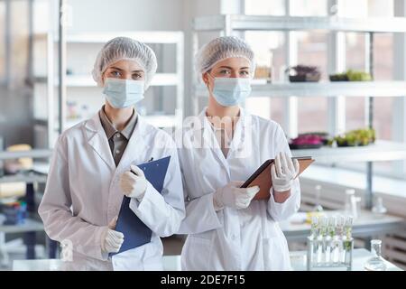 Ritratto in vita di due scienziati femminili che indossano una maschera facciale e tenere le lavagne mentre si è in piedi in laboratorio medico Foto Stock