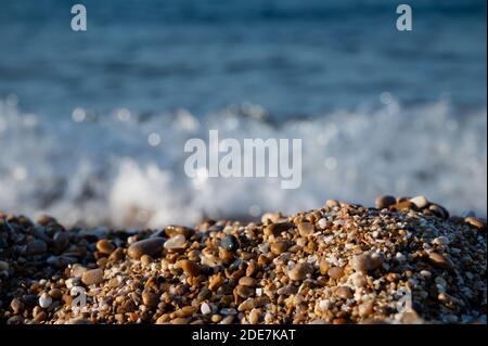 Ciottoli colorati umidi da vicino con luce del tramonto dorata e mare fuori fuoco sullo sfondo Foto Stock