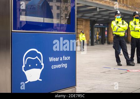 Segnale di avvertimento alla stazione di Kings Cross che insegna a indossare una copertura facciale a un COVID 19, con la polizia pronta per la protesta anti-blocco marcia a Londra, Regno Unito Foto Stock