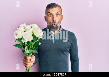 Bell'uomo di mezza età che tiene bouquet di fiori bianchi spaventati e stupiti con bocca aperta per sorpresa, viso incredulo Foto Stock