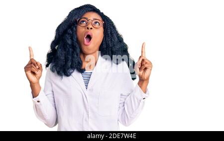 Bella donna opticista afroamericana con occhiali da optometria stupita e sorpresa guardando in su e puntando con le dita e le braccia sollevate. Foto Stock