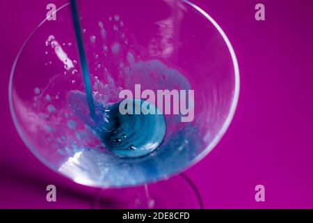 il liquido blu viene versato in un bicchiere martini da cocktail uno sfondo rosa Foto Stock