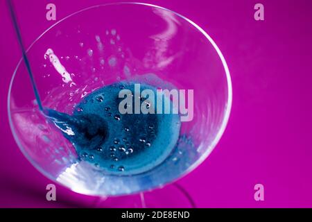 il liquido blu viene versato in un bicchiere martini da cocktail uno sfondo rosa Foto Stock