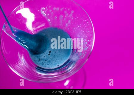 il liquido blu viene versato in un bicchiere martini da cocktail uno sfondo rosa Foto Stock