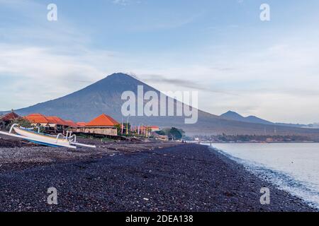 Vista del vulcano Agung dall'oceano. Villaggi, case tradizionali barche da pesca jukung intorno a. Amed, Karangasem Regency, Bali, Indonesia Foto Stock