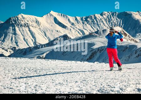 Donna sciatrice sportiva scattando una foto con il telefono dalle montagne innevate e dalla stazione sciistica invernale. Felice sciatrice che gode della vista, Francia, Europa Foto Stock