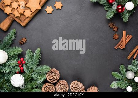 Sfondo della cornice di Natale con spazio di copia. Biscotti di pan di zenzero, coni, spezie e abete decorato festoso su cemento nero Foto Stock