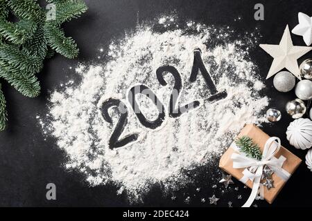 2021 simbolo del nuovo anno scritto con farina su fondo nero di cemento con Natale, decorazioni di Capodanno abete albero, giocattoli color argento, carta artigianale g Foto Stock