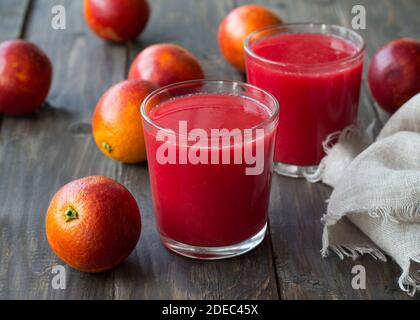 Spremuta fresca di arance di sangue in bicchieri con arance fresche intere su un tavolo di legno, fuoco selettivo Foto Stock