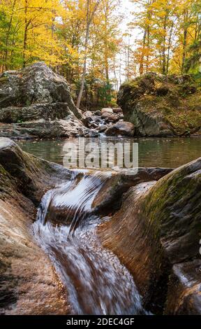 Ruscello che scende tra grandi massi in una piscina di cristallo smeraldo. Piscina sul fiume Mad. Alberi che cambiano colore in autunno. Warren, VT, Stati Uniti Foto Stock