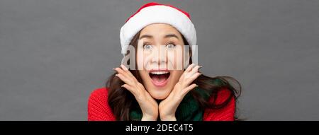 Sorpresa eccitato bella donna asiatica in rosso maglione di Natale e. hat making wow gesture studio girato su sfondo grigio banner Foto Stock