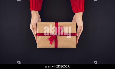 Mani donna che danno scatola regalo ai braccisas con parte superiore di prua rossa vista su sfondo nero Foto Stock