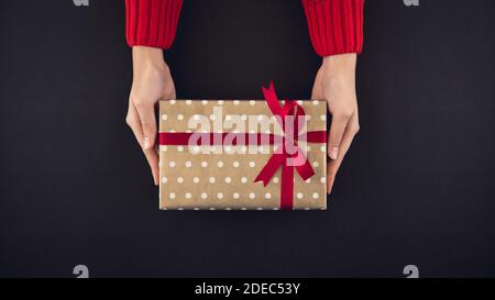 Le mani della donna danno ai braccisas la vista dall'alto della scatola regalo su nero sfondo Foto Stock