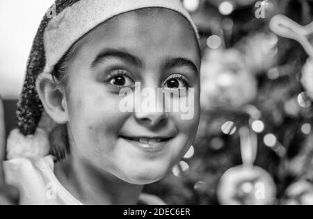 Felice ragazza sorridente che indossa Santa Hat a casa davanti all'albero di Natale. Foto Stock