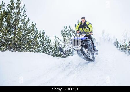 Saltando su una motoslitta sullo sfondo di una foresta invernale. Motoslitta brillante. Atleta in motoslitta che si muove nella foresta invernale in montagna. Uomo Foto Stock