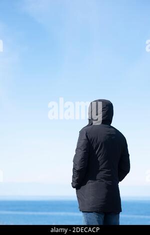 Vista posteriore della figura con cappuccio in piedi sulla spiaggia Foto Stock