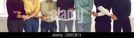 Gruppo di persone diverse che si levano in piedi insieme e che tengono le mani mostrando la loro unità Foto Stock