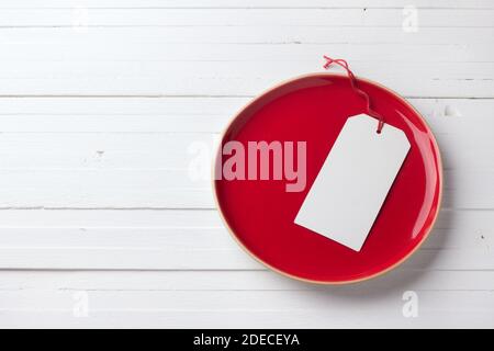 Piatto rosso vintage con etichetta bianca vuota su a. sfondo bianco Foto Stock