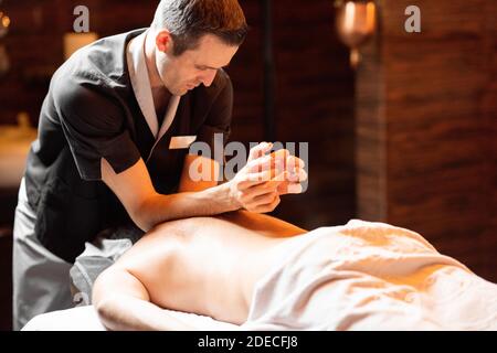 Massaggiatore professionista che fa un massaggio profondo della schiena ad un maschio Cliente al salone Spa Foto Stock