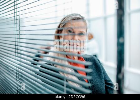 donna di affari riuscita che guarda attraverso le persiane della finestra. Foto Stock