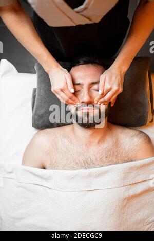L'uomo bearded riceve un massaggio facciale, distendendo al salone di bellezza, vista dall'alto Foto Stock