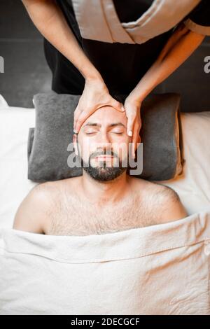 L'uomo bearded riceve un massaggio facciale, distendendo al salone di bellezza, vista dall'alto Foto Stock