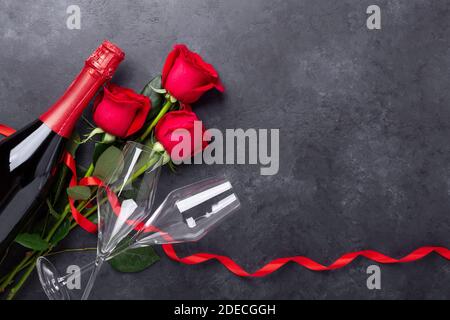 Biglietto d'auguri per San Valentino. Rose rosse, champagne, bicchieri su sfondo di pietra. Vista dall'alto - immagine Foto Stock