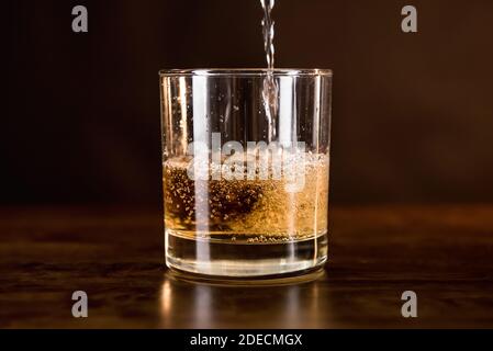 Una bevanda a base di whisky versata nel bicchiere di legno bancone bar - concetto di bevande alcoliche e alcoliche Foto Stock