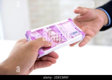 Uomo d'affari che consegna il wad della nuova banconota da rupee indiana croccante soldi al suo partner contro sfondo bianco sfocato Foto Stock