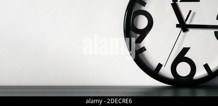 Orologio moderno minimalista o semplice bianco e nero su tavolo di legno nero e parete bianca con spazio per il testo. Banner orizzontale lungo Foto Stock