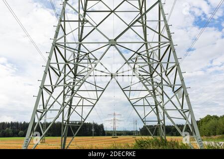 Oberbrunn, Germania - 23 agosto 2020: Vista attraverso e lungo una linea elettrica aerea. Simbolo per energia, trasmissione di energia e rete elettrica. Foto Stock