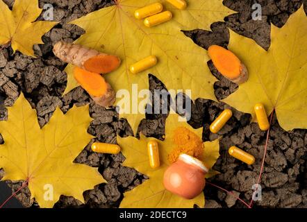 Sughero piano di fondo con curcuma in forme diverse Capsule e. polvere in una mini pentola arancione e radice tagliata in pezzi Foto Stock