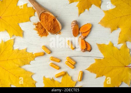 Fondo piatto con curcuma in diverse forme capsula e polvere in un cucchiaio di legno e radice tagliata a pezzi Foto Stock