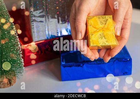 Le mani dei giovani donne che tengono una scatola di regalo circondata da regalo scatole e albero di natale Foto Stock