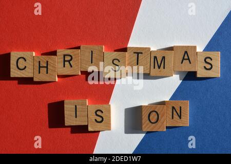Natale è in corso, parole in lettere alfabetiche in legno isolato su sfondo rosso, bianco e blu Foto Stock