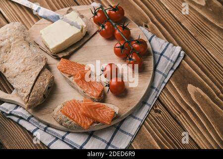 Due panini con salmone affumicato e altro cibo sulla vecchia tavola su rustico sfondo di legno. Vista dall'alto Foto Stock