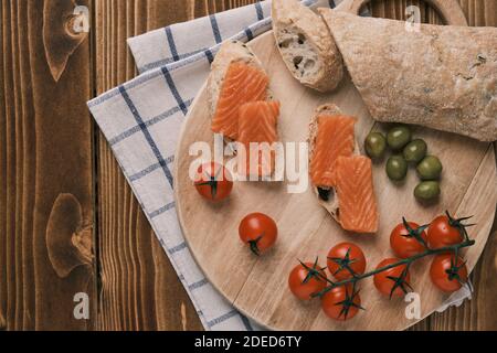 Due panini con salmone affumicato e altro cibo sulla vecchia tavola su rustico sfondo di legno. Vista dall'alto Foto Stock