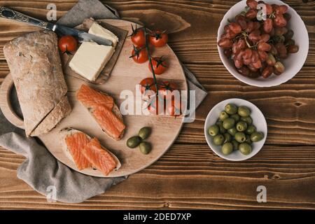 Due panini con salmone affumicato e altro cibo sulla vecchia tavola su rustico sfondo di legno. Vista dall'alto Foto Stock