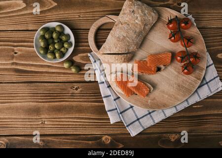 Due panini con salmone affumicato e altro cibo sulla vecchia tavola su rustico sfondo di legno. Vista dall'alto Foto Stock