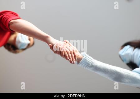 Due donne in maschere mediche protettive scuotono le mani Foto Stock
