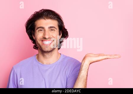 Primo piano ritratto di giovane ragazzo sorriso braccio palma mostrando prodotto vestito viola isolato su sfondo di colore rosa Foto Stock