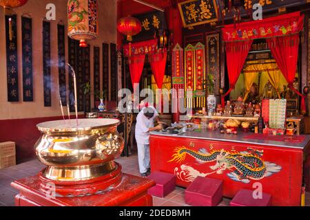 Interni o un tempio cinese a Malacca, Malesia con bastoni di smoking in primo piano e una persona che pulisce Foto Stock