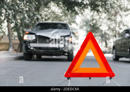 Cartello rosso triangolo di arresto di emergenza sulla strada in scena di incidente d'auto. Auto SUV rotta su strada a caso di incidente stradale. Incidente stradale in caso di incidente stradale su strada urbana Foto Stock