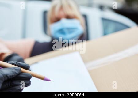 Servizio di consegna il vettore pacchi con maschera facciale richiede la conferma per firma Foto Stock