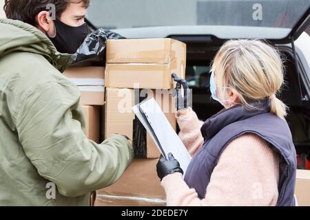 Il reparto merci in entrata controlla la bolla di consegna dei pacchi per pacchetti dal servizio pacchi con maschera facciale a causa di Covid-19 Foto Stock