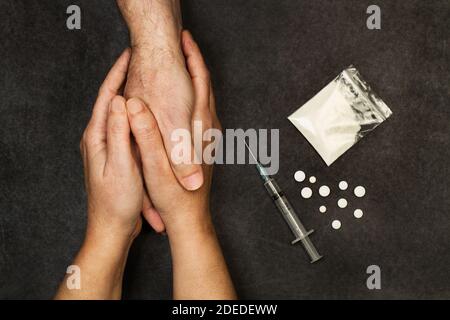 Mani di donna che tengono la mano di un uomo addicted sopra uno sfondo scuro Foto Stock