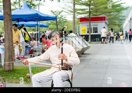 Musicista di strada cinese di mezza età che suona lo strumento musicale cinese tradizionale Erhu (violino cinese) nel Central Park di Shenzhen, Cina Foto Stock